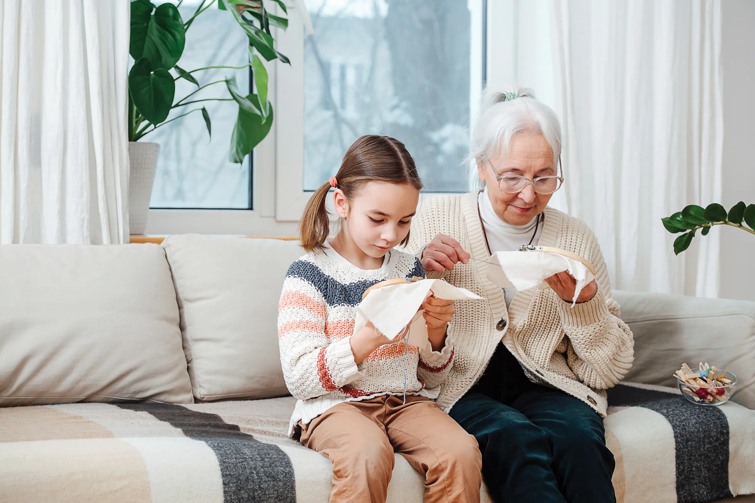 senior woman and her granddaugter doing cross-stitch on a couch