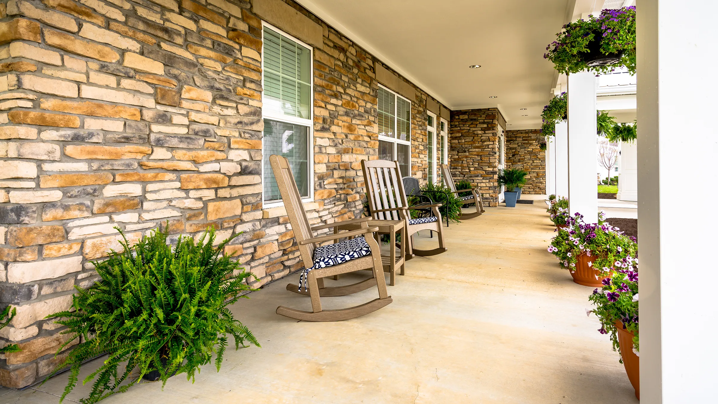 front porch of senior living facility with rocking chairs and colorful plants both hanging and planted on the ground