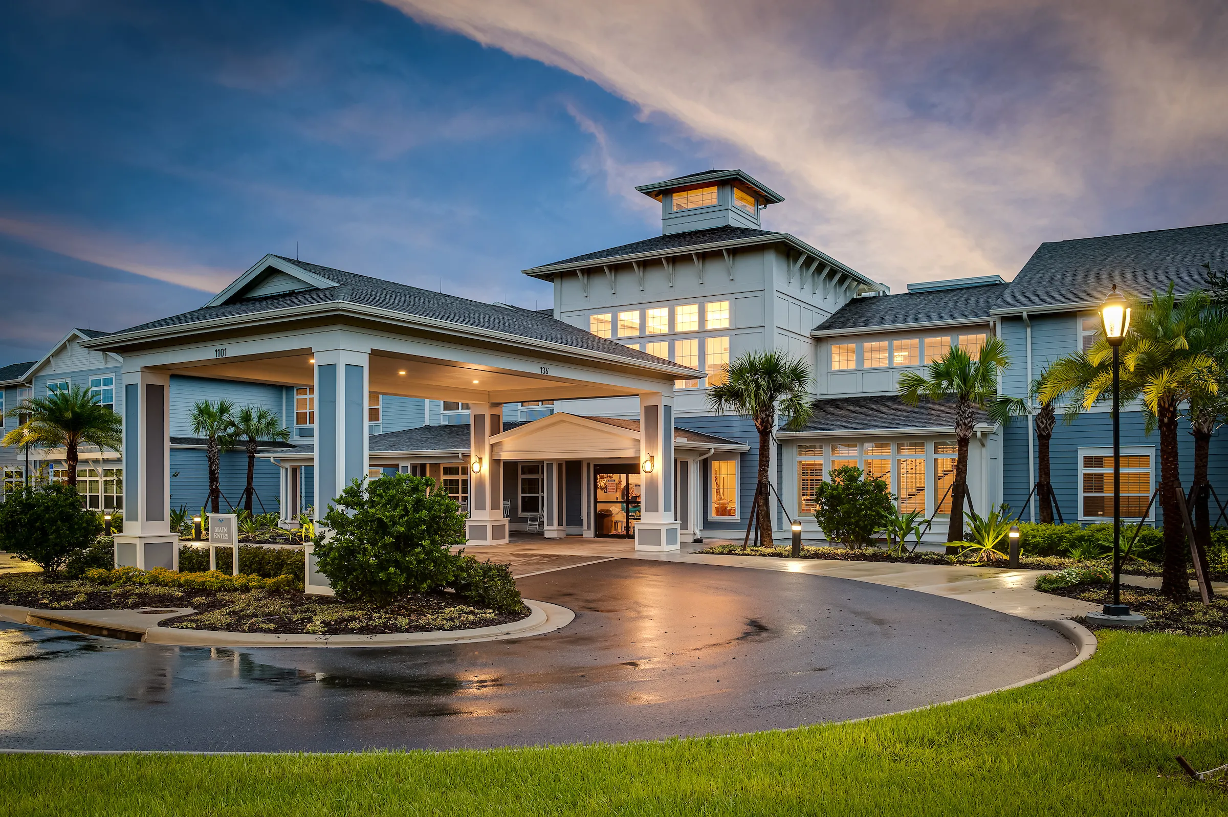 exterior of two story senior living community at night with palm trees in florida
