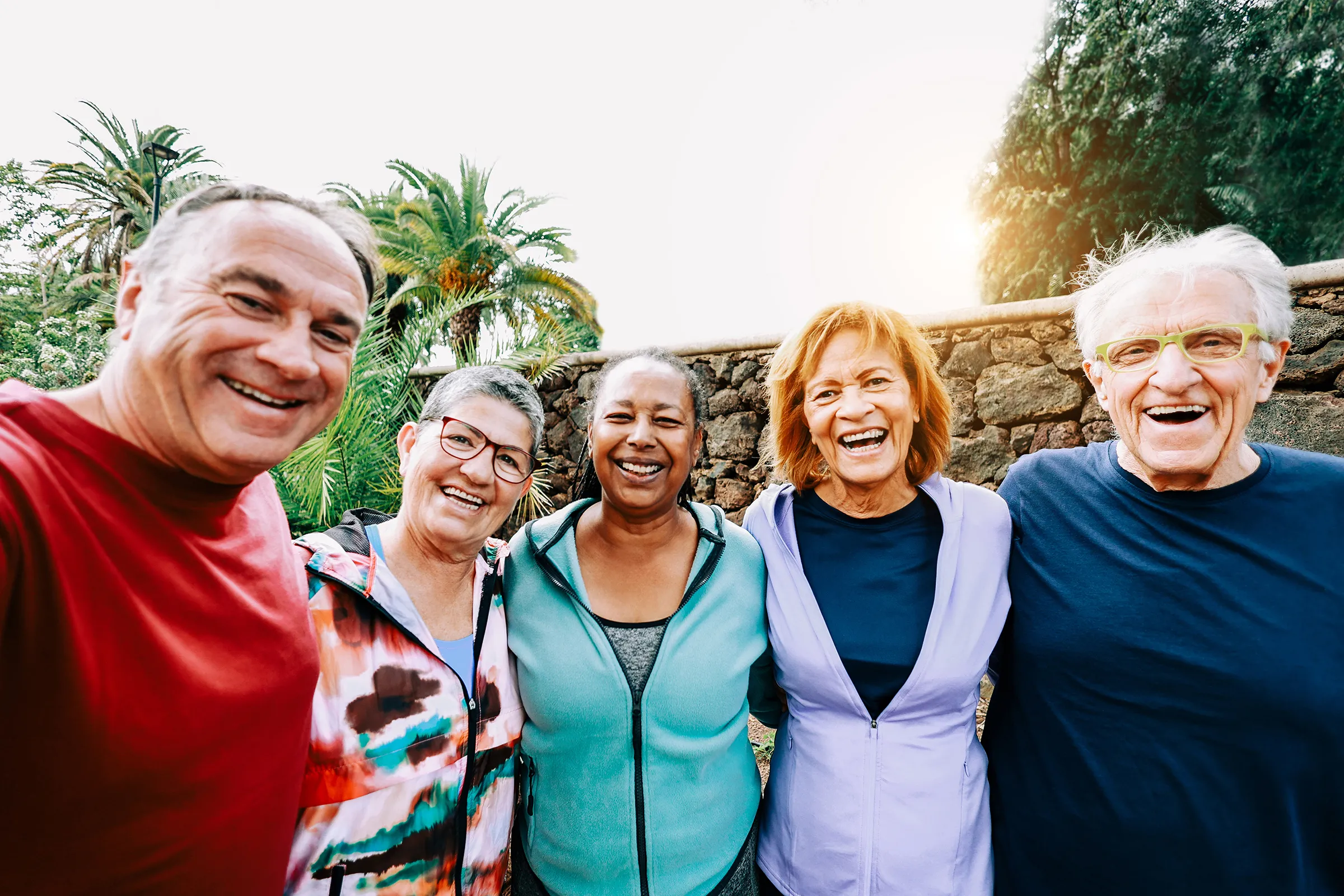 group of senior citizens outside smiling in front of stone wall and palm trees