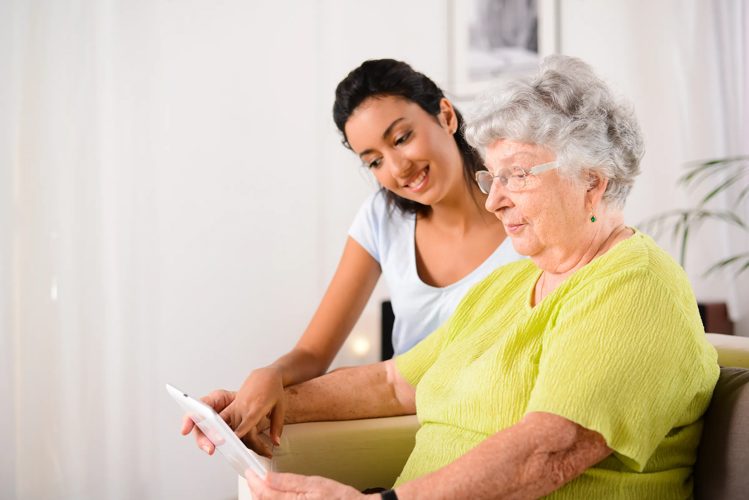 woman helping senior with ipad in memory care facility