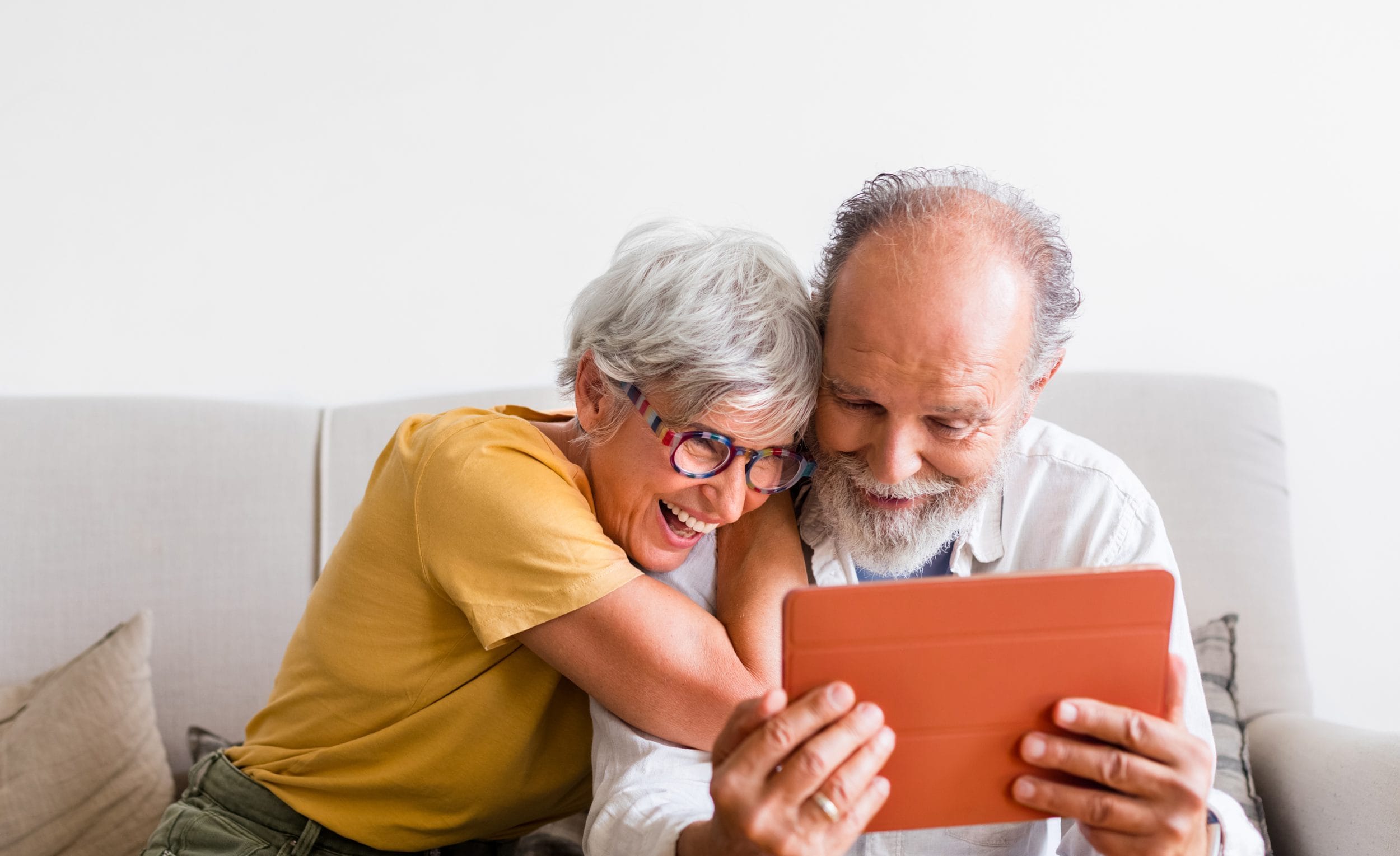senior couple on couch smiling with ipad