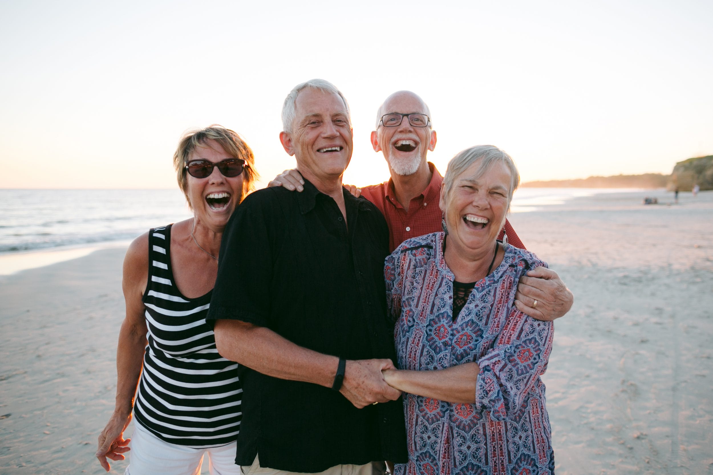group of older adults laughing and embracing on beach